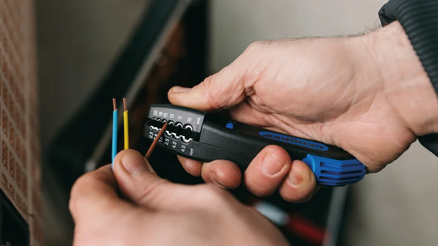 Ein Elektriker entfern am ende unterschiedlicher Kabel mit einer Abisolierzange Isolierung