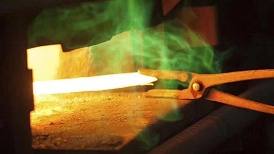 Glühendes Metallstück wird mit einer Schmiedezange aus einer Umformvorrichtung entnommen